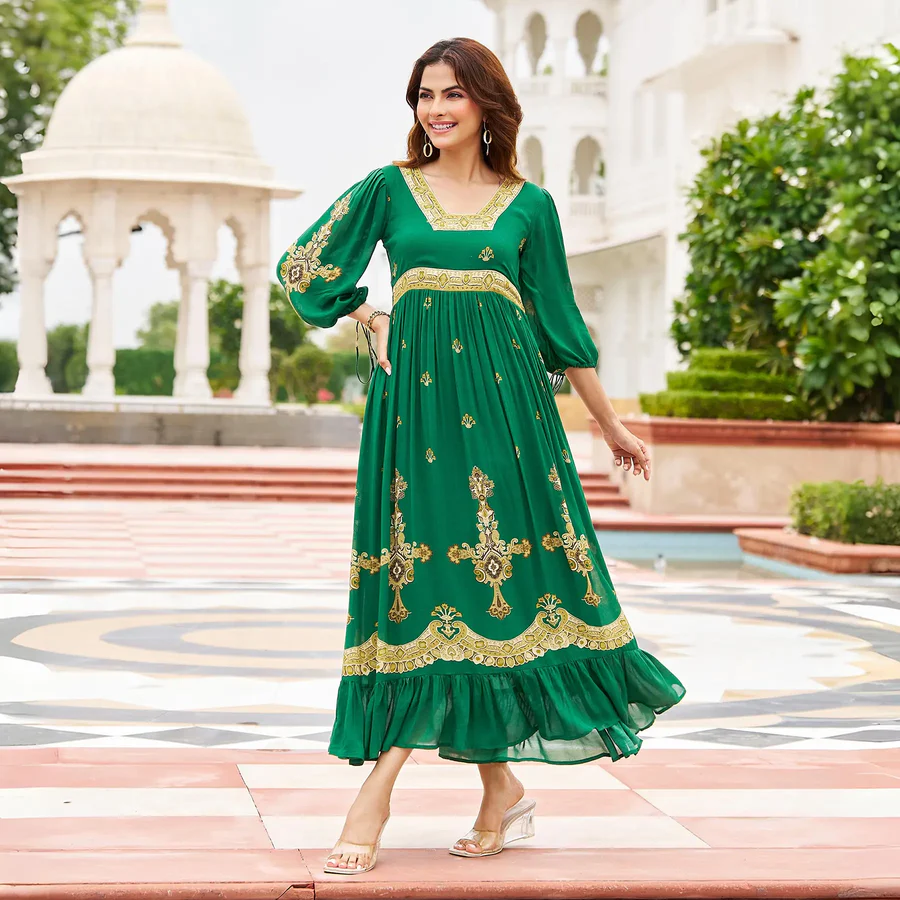 Woman wearing a green embroidered A-line maxi dress with golden detailing and flared hem, standing in an outdoor palace-style setting.